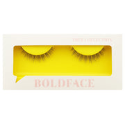 The Short and Sweet false eyelashes by Boldface are presented in a white rectangular box featuring a clear display window. The cruelty-free lashes are highlighted against a vibrant yellow backdrop. The packaging is adorned with